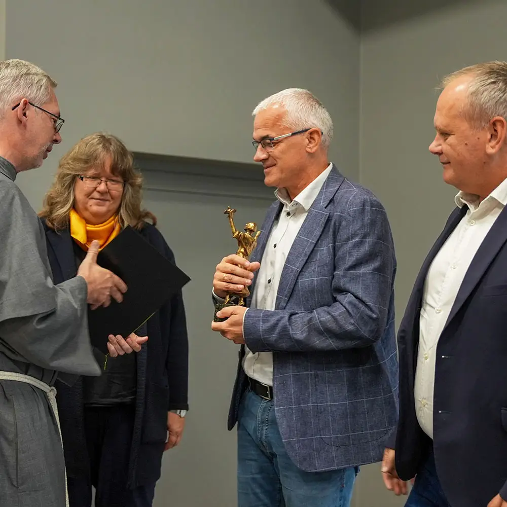 Przedstawiciele Domu Wydawniczego Rafael odbierają statuetkę św. Franciszka podczas święta krakowskiej prowincji franciszkanów w Harmężach