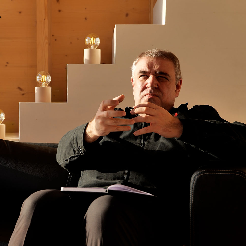 Ks. Robert Woźniak siedzi na kanapie i gestykuluje, omawiając Trójcę Świętą i liturgię jako dzieło Trójcy.